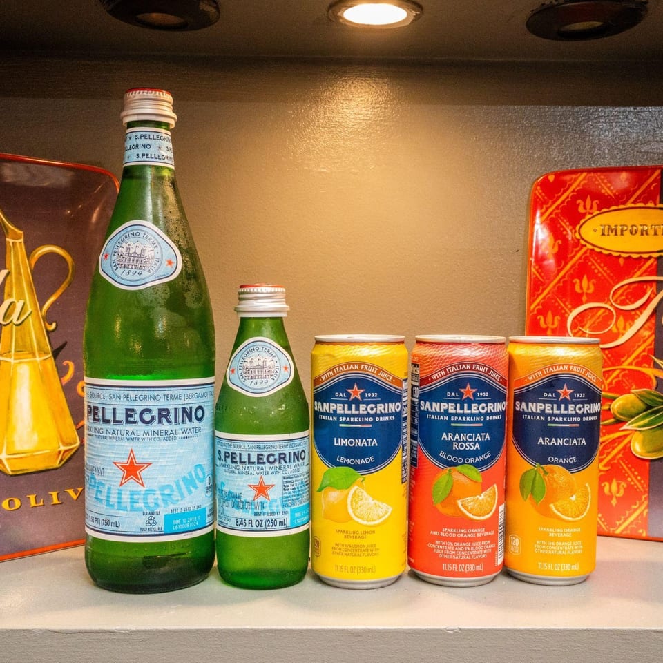 Assortment of San Pellegrino sparkling water bottles and flavored sparkling drink cans on a counter.