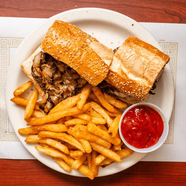 Cheesesteak sandwich with caramelized onions and melted cheese, served with golden french fries and ketchup.