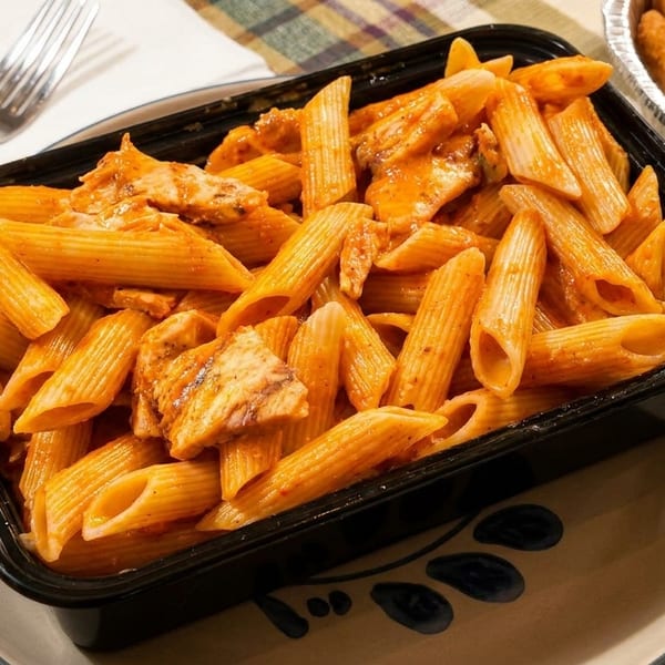 Penne pasta with chicken in a creamy red sauce, served in a black container.