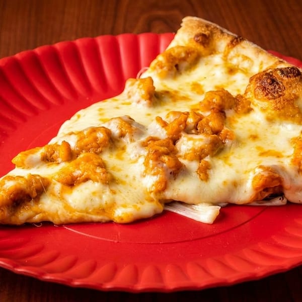 A slice of buffalo chicken pizza with melted cheese and orange chicken pieces on a red plate.