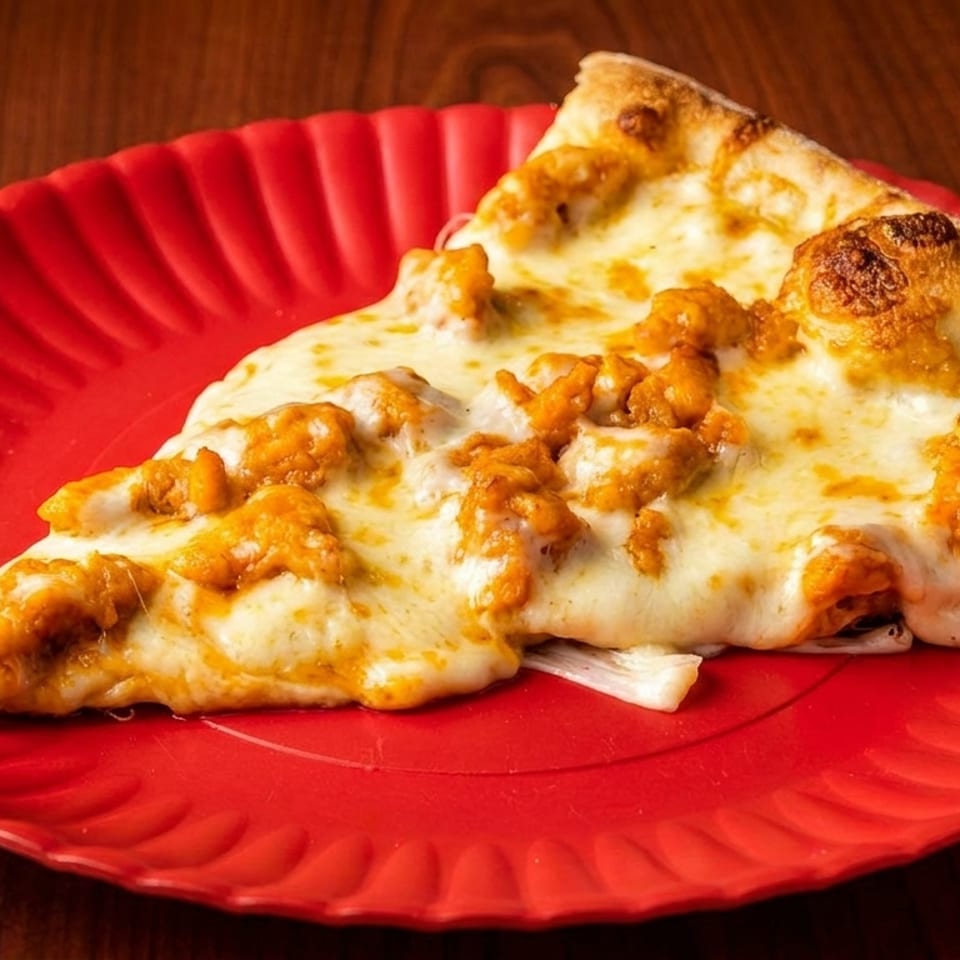 A slice of buffalo chicken pizza with melted cheese and orange chicken pieces on a red plate.