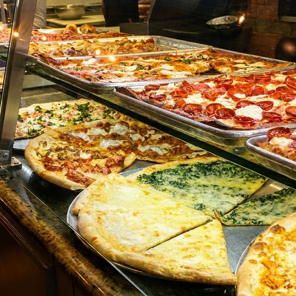 A glass display case filled with various pizzas, including pepperoni, cheese, and spinach, at a pizzeria.